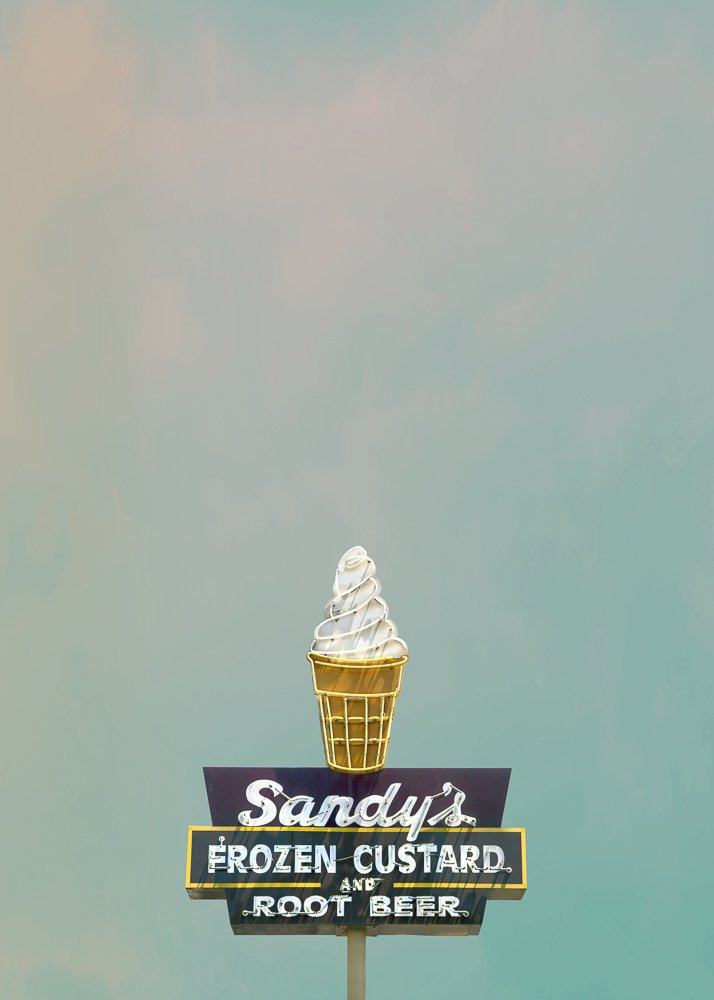 Sandys Ice Cream Austin Texas sign featuring frozen custard cone and root beer advertisement against blue sky background