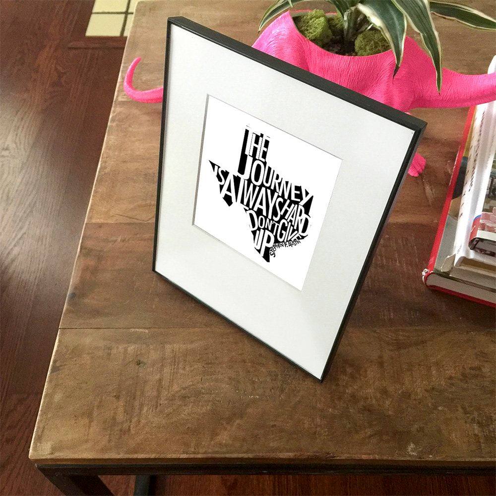 Stephen F. Austin Quote framed art print with motivational text "The Journey is Always Hard, Don't Give Up" in Texas-shaped design on wooden table