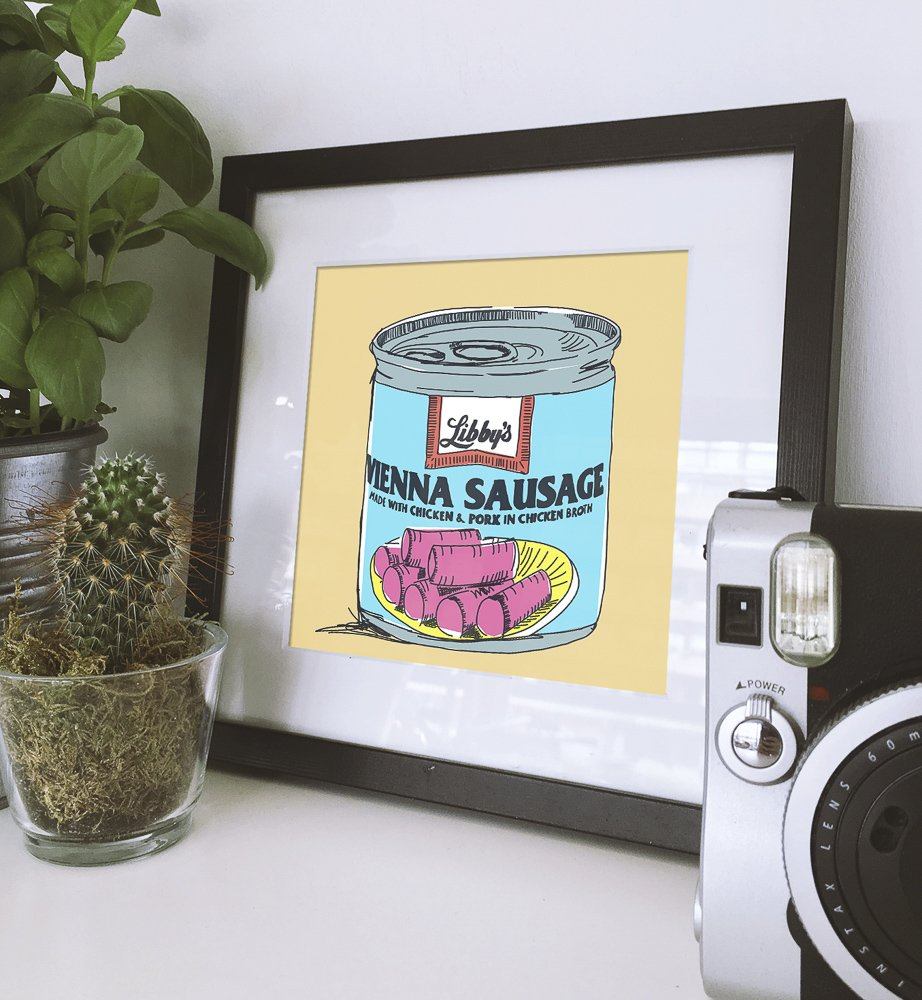 Framed vintage-style Vienna Sausage can print with plants and camera on white surface