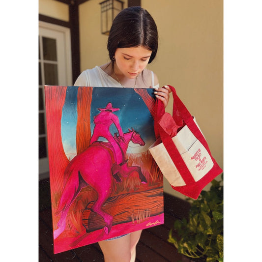 Property of the City of Fort Worth red canvas boat tote by Crum Art, held beside a Caya Crum painting of a pink horse and rider