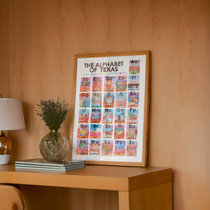 Alphabet of Texas Icons Texas Art print by Caya Crum — framed in a wood-accent room