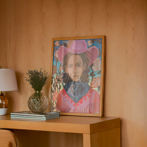 Cowgirls & Flowers cowgirl art print by Caya Crum — framed in a wood-accent room