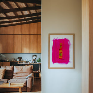 Cholula Hot Sauce kitchen art print by Caya Crum — framed in a wood-accent room