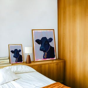 Money Cow pink pop art print by Caya Crum — framed in a wood-accent room