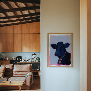 Money Cow black cow art print by Caya Crum — framed in a wood-accent room