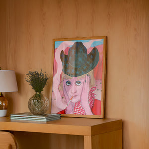 Emma cowgirl art print by Caya Crum — framed in a wood-accent room