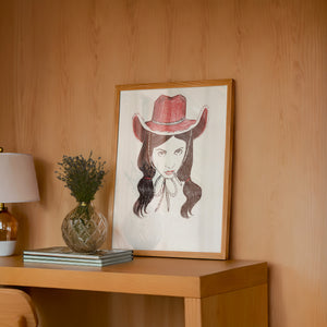 Tavi cowgirl art print by Caya Crum — framed in a wood-accent room