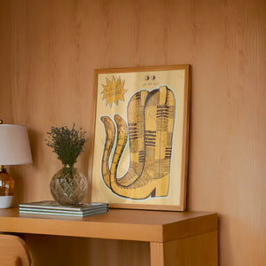 Roach Stompers cowboy boot art print by Caya Crum — framed in a wood-accent room