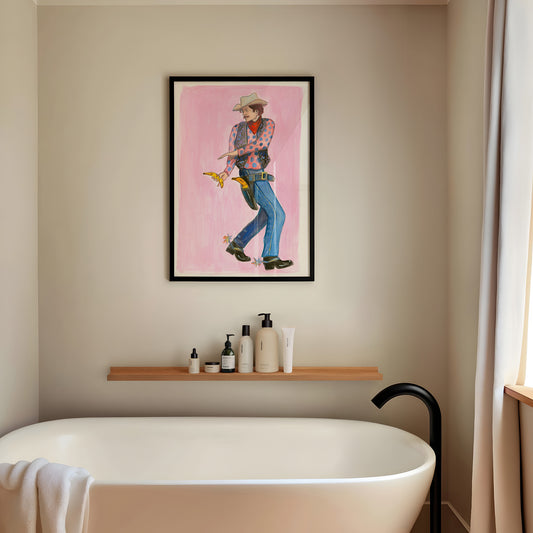 Banana Cowboy Bandit art print by Caya Crum — a cowboy in a blue polka dot shirt drawing a banana, framed on a wall