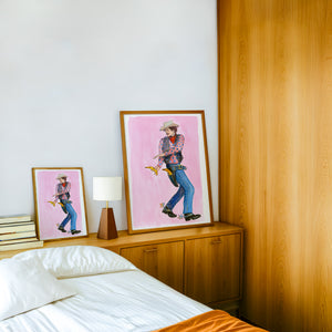 Banana Guns cowboy art print by Caya Crum — framed in a wood-accent room