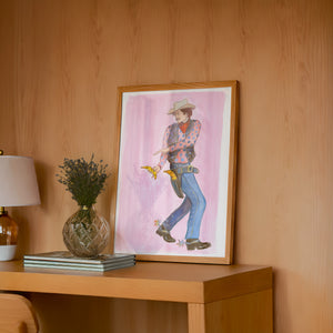 Banana Guns cowboy art print by Caya Crum — framed in a wood-accent room