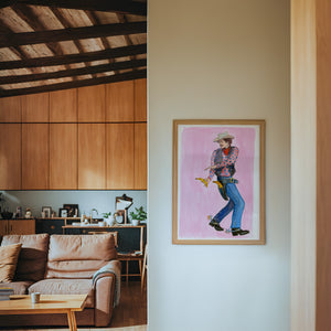 Banana Guns cowboy art print by Caya Crum — framed in a wood-accent room
