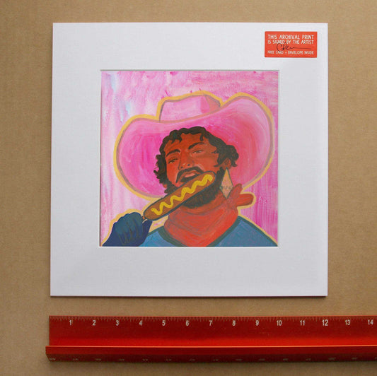 Corndog Cowboy Print by Caya Crum featuring a cowboy eating a corndog with pink background and hat, fine art giclee on cotton rag paper