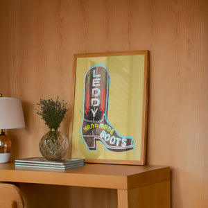 Leddy Boot Ochre cowboy boot art print by Betsy Crum — framed in a wood-accent room