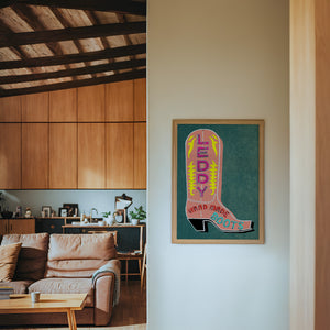 Leddy Boots Pink cowboy boot art print by Betsy Crum — framed in a wood-accent room