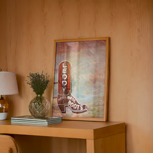 Leddy Boots Big Sky cowboy boot art print by Betsy Crum — framed in a wood-accent room
