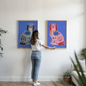 Good Luck Staffordshire dog print pair by Caya Crum being hung side by side on a living room wall