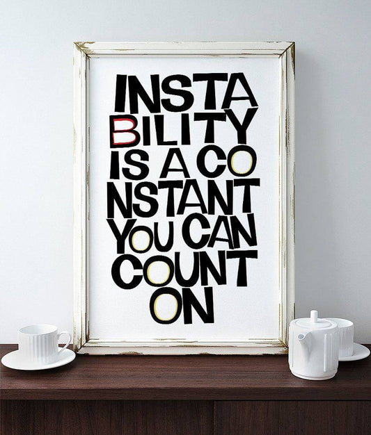Framed museum print with bold black text reading "Instability Is A Constant You Can Count On" with some letters in red and yellow on acid-free cotton paper.