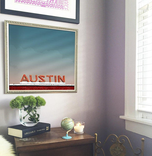 Framed museum print of Austin Real World building in Texas displayed on a wall above a wooden desk with decorative items.