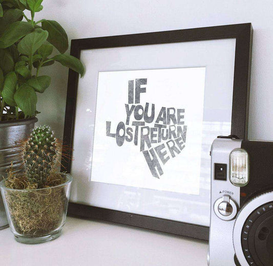 Framed Texas Shape Art Print with "If You Are Lost Return Here" text on white cotton rag paper next to plants and camera