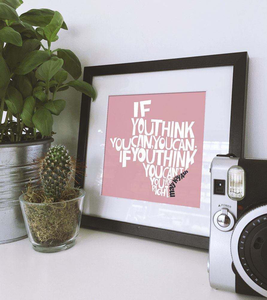 Mary Kay Ash art print with motivational quote in black frame on white table with plants and retro camera