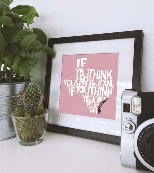 Mary Kay Ash art print with motivational quote in black frame on white table with plants and retro camera