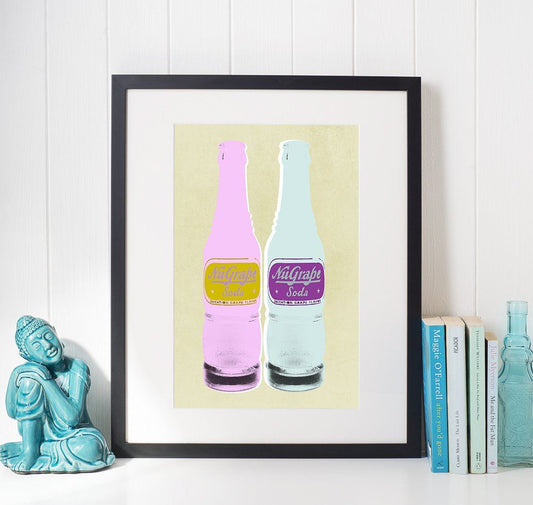 Framed pop art print of two vintage NuGrape soda bottles in pastel colors displayed on a wall next to books and a turquoise Buddha sculpture