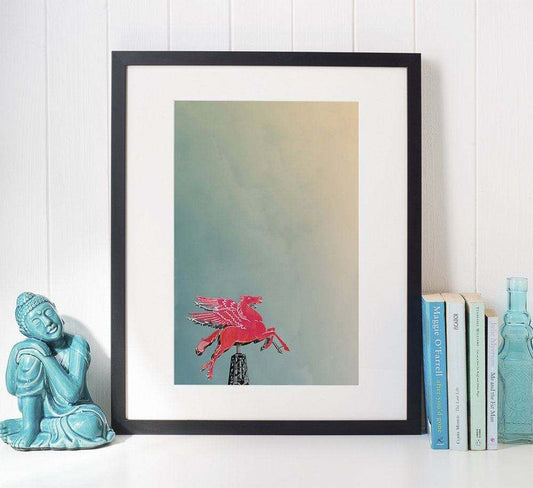 Dallas Texas Pegasus art print by Betsy Crum in black frame on shelf with decorative statue and books