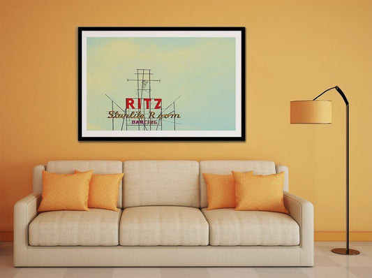Framed Ritz Starlite Room museum print above beige sofa with orange cushions in modern living room