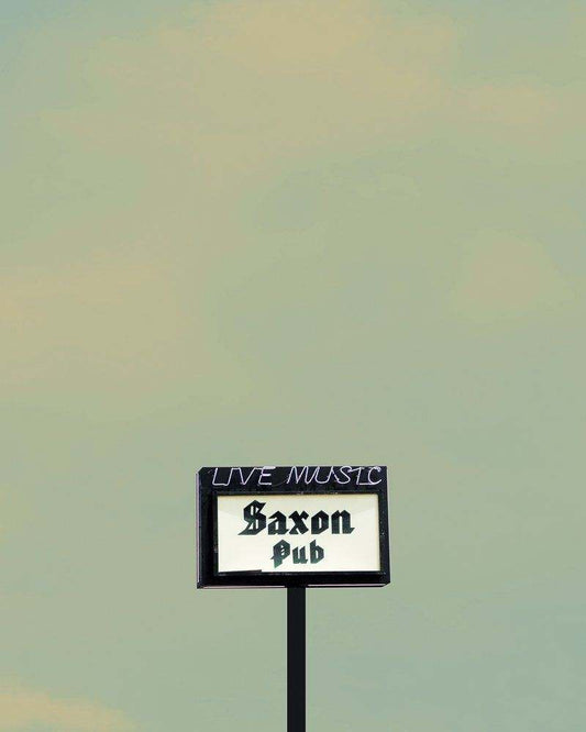 Saxon Pub Art Print by Betsy Crum showcasing vintage pub sign with Live Music text on muted sky background