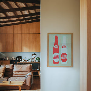 Big Red Two Bottles kitchen print by Betsy Crum — framed in a wood-accent room
