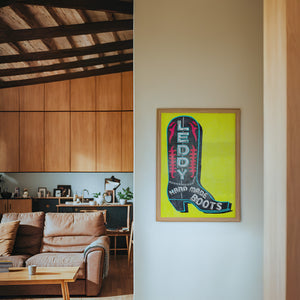 Leddy Boot Yellow cowboy boot art print by Betsy Crum — framed in a wood-accent room