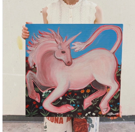 Caya Crum holding the Pink Unicorn original painting in the studio