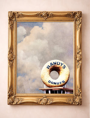 Randy's Donuts Los Angeles art print by Betsy Crum in a vertical gold frame, the giant donut sign under a big cloudy sky