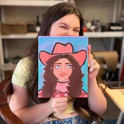 Smoking Cowgirl Portrait Workshop — a painter holding her finished pink-hat cowgirl portrait